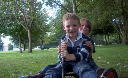 Two happy children sliding a grassy hill on a sledge